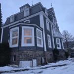 House with black gabled roof and white windows, surrounded by snow and trees.