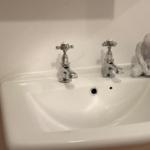 White sink with two faucets and a sculpture beside it.