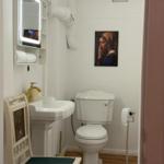 Bathroom with toilet, sink, and mirror cabinet. Wall painting and wooden floor.