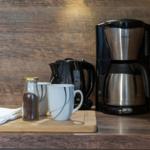 Kaffeemaschine, Kanne, Tassen und Kaffeebohnen auf Holzoberfläche.