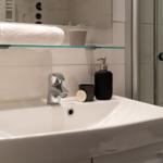 Bad mit Waschbecken, Spiegel und Dusche. Auf der Ablage liegt ein Handtuch.