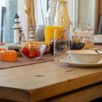 Frühstückstisch mit Obst, Getränken und Geschirr vor Fenster mit Leuchtturmdekoration