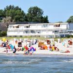 Strand mit bunten Strandkörben und Menschen. Im Hintergrund stehen Ferienhäuser.
