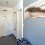 Flur mit Wandbild, Spiegel und Garderobe. Bodenfliesen und blaue Wand.