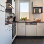 Moderne Küche mit weißen Schränken, Edelstahlgeräten und dunklem Arbeitsplatz.