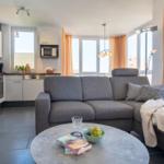 Wohnbereich mit Sofa, Küchenzeile und großen Fenstern.