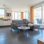 Wohnung mit Küche, Sofa und Balkon mit Stühlen.