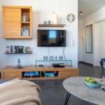 Wohnzimmer mit TV, Bücherregal und Esstisch. Wanduhr und Dekoration sichtbar.