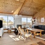 Living room with wooden walls, sofa, table, and fireplace. Large windows with view of outdoor area.