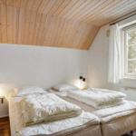 Zimmer mit zwei Betten, Holzdecke und Fenster mit Blick auf Bäume.