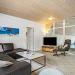 Wohnzimmer mit Sofa, Fernseher und Kaminofen. Glaswand zeigt Pool.