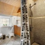 Badezimmer mit Dusche, Toilette und Waschbecken unter Holzdecke.