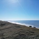 Meer und Strand aus der Dünenlandschaft mit klarem Himmel.