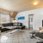 Wohnzimmer mit Sofa, Sessel und Fernseher. Holzdecke und große Fenster.