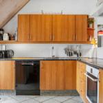 Küche mit Holzschränken, Spüle und Kochfeld. Geräte wie Kühlschrank und Mikrowelle vorhanden.