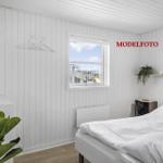 Schlafzimmer mit weißem Bett, Fenster und Holzboden. An der Wand hängt ein Kleiderhaken.
