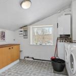 Room with washing machine, boiler, and wooden cabinet. Window overlooking outdoor area.