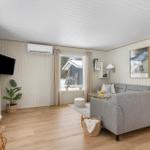 Living room with gray sofa, wooden floor, and white walls. Windows with view outside.