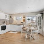 Kitchen with dining table, white cabinets, and wooden floor. Large windows and light walls.