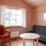 Wohnzimmer mit Sofa, Rattan-Stuhl und runden Tisch. Holzwände und Fenster mit weißen Vorhängen.
