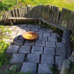 Gartenbereich mit Steinplatten, Holzumrandung und runden Metalltopf.