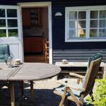 Terrasse mit Tisch, Stühlen und Blick ins Haus. Holztisch, Stühle mit Kissen.