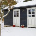 Schwarzes Holzhaus mit zwei weißen Türen und Schneebedeckten Pflanzen.