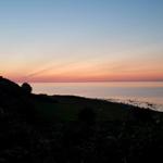 Sonnenuntergang über Meer und Hügeln mit Bäumen im Vordergrund