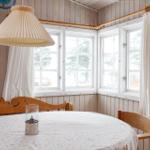 Rundtisch mit Tischdecke und Holzstühle vor Fenstern mit weißen Vorhängen.