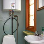 Badezimmer mit Toilette, Waschbecken und Wasserheizer an der Wand.