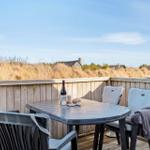 Terrasse mit Tisch und Stühlen, Blick auf Dünen und Häuser im Hintergrund.