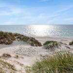 Strand mit Dünen und Meer unter blauem Himmel.