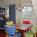 Küche mit Essbereich, blauen Schränken und farbigen Stühlen.