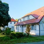 Ein weißes Fachwerkhaus mit rotem Dach und blauen Fensterläden in grüner Umgebung.