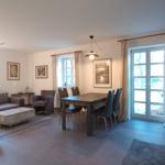 Wohn- und Essbereich mit Sofa, Tisch und Stühlen. Fenster und Glastür mit Vorhängen.