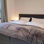 Schlafzimmer mit Doppelbett, Nachttischen und Pflanze am Fenster.