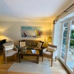 Wohnzimmer mit Sofa, zwei Sesseln und Glas-Tür zu Außenbereich.