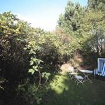 Garten mit weißem Tisch, Stühlen und Strandkorb. Umgeben von grünen Sträuchern und Bäumen.