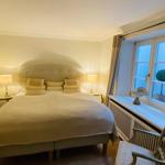 Schlafzimmer mit Bett, zwei Nachttischen und Lampe, Fenster mit Vorhang und Stuhl.