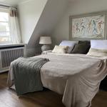 Schlafzimmer mit Dachschrägen, Bett, Fenster und Wandbild.