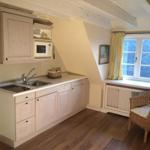 Küche mit Arbeitsplatte, Spüle und Mikrowelle. Fenster mit gelben Vorhängen und Stuhl.