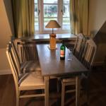 Esszimmer mit Holztisch, vier Stühlen und Fenster mit Gardinen.