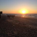 Sonnenuntergang am Strand mit Holzsteg und sanften Wellen.