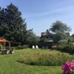 Grüner Garten mit Sitzgelegenheiten und traditionellem Haus im Hintergrund.