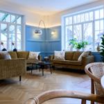 Wohnzimmer mit blauen Wänden, Holzboden und zwei Sofas. Große Fenster und Pflanzen sorgen für viel Licht.