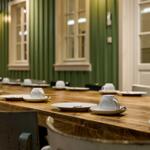 Langtisch mit Tassen und Tellern in einem Raum mit grünem Holzpaneelen und Fenstern.