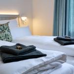 Zwei Betten mit weißen Laken und dunklen Handtüchern. Fenster mit blauen Vorhängen.