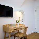 Schreibtisch mit Stuhl, Fernseher und Lampe in einem Raum mit Holzboden und weißer Tür.