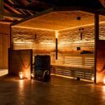 Sauna mit Holzwand und Glasfront, Beleuchtung und Bänken sichtbar.