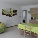 Wohn- und Essbereich mit grünem Sofa, Tisch mit Tischdecke und Küchenzeile.